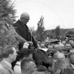 Uroczystość ofiarowania Premierowi RP Waleremu Sławkowi zagrody w Racławicach. Jan Piwnik z zasłoniętą twarzą poniżej mikrofonu, Racławice 5 VII 1935 r. / NAC