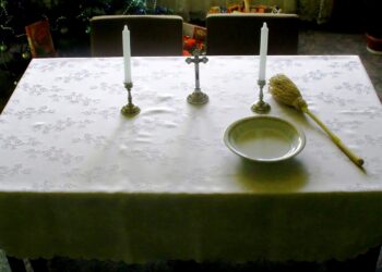 Stół przygotowany na wizytę duszpasterską: świece, kropidło, krzyż, woda święcona. Wizyta duszpasterska. Kolęda / wikipedia.org