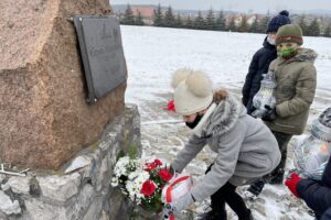 31.01.2021. Bilcza. Cmentarz parafialny. Dzieci z klasy III składają kwiaty i zapalają znicze pod tablicą poświęconą ks. Piotrowi Ściegiennemu / Kamil Król / Radio Kielce