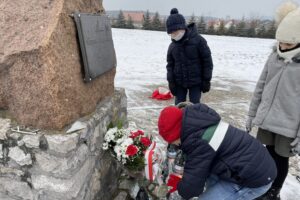 31.01.2021. Bilcza. Cmentarz parafialny. Dzieci z klasy III składają kwiaty i zapalają znicze pod tablicą poświęconą ks. Piotrowi Ściegiennemu / Kamil Król / Radio Kielce