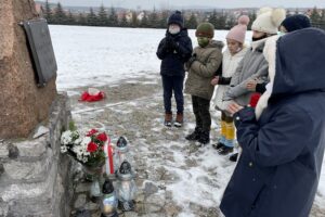 31.01.2021. Bilcza. Cmentarz parafialny. Dzieci z klasy III składają kwiaty i zapalają znicze pod tablicą poświęconą ks. Piotrowi Ściegiennemu / Kamil Król / Radio Kielce