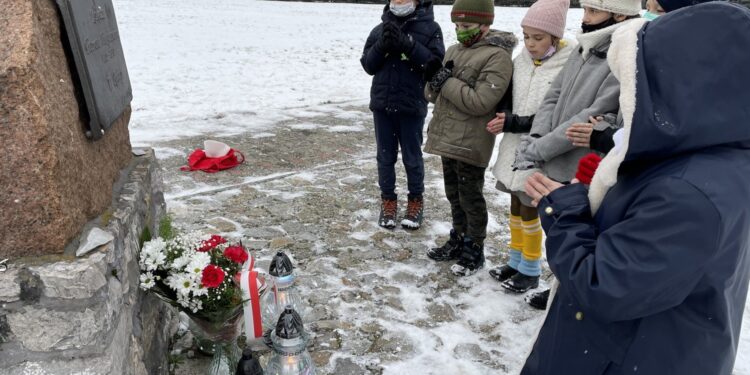 31.01.2021. Bilcza. Cmentarz parafialny. Dzieci z klasy III składają kwiaty i zapalają znicze pod tablicą poświęconą ks. Piotrowi Ściegiennemu / Kamil Król / Radio Kielce