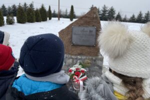 31.01.2021. Bilcza. Cmentarz parafialny. Dzieci z klasy III składają kwiaty i zapalają znicze pod tablicą poświęconą ks. Piotrowi Ściegiennemu / Kamil Król / Radio Kielce