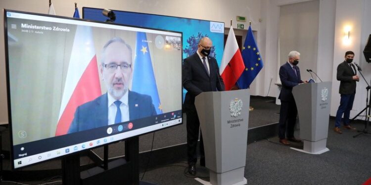 07.12.2021. Warszawa. Minister zdrowia Adam Niedzielski (na ekranie), wiceminister zdrowia Waldemar Kraska (z prawej) i Główny Inspektor Sanitarny wz. Krzysztof Saczka (z lewej) podczas konferencji prasowej w siedzibie Ministerstwa Zdrowia / PAP/Wojciech Olkuśnik