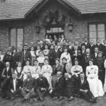 Car, cesarz, król i papież na peronie w Bzinie - Radio Kielce Grupa pracowników kolei z rodzinami przed wejściem do szpitalika kolejowego zbudowanego na początku XX wieku przy przejeździe kolejowym. Zdjęcie wykonane przez zakład fotograficzny Stanisławy Odembskiej w Kamiennej