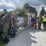 10.08.2023. Mokrsko Dolne. Delegacja 58. Marszu Szlakiem Pierwszej Kompanii Kadrowej złożyła wieńce i zapaliła znicze przed pamiątkową tablicą wmurowaną w kościelny mur / Fot. Krzysztof Bujnowicz - Radio Kielce