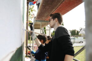 26.09.2024. Masłów. Uczniowie pod okiem artysty Mikołaja Korusa malują mural przedstawiający poetę Jana Kochanowskiego na budynku Szkoły Podstawowej w Brzezinkach / Fot. Wiktor Taszłow - Radio Kielce