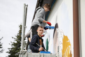 26.09.2024. Masłów. Uczniowie pod okiem artysty Mikołaja Korusa malują mural przedstawiający poetę Jana Kochanowskiego na budynku Szkoły Podstawowej w Brzezinkach / Fot. Wiktor Taszłow - Radio Kielce