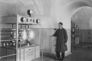 Pracownik przy aparaturze nadawczej (oscylatorze) z lampami elektronowymi dużej mocy w pomieszczeniach Fortu Mokotowskiego. 1927 rok / źródło: Narodowe Archiwum Cyfrowe